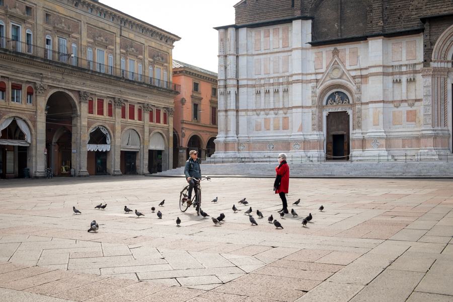 March 13th 2020, Bologna (Italy). In an unusually empty Piazza Maggiore (the city's main square) an encounter between a man and a woman is held keeping the safety distance imposed by the Italian authorities as a measure to fight the coronavirus (Covid-19) outbreak. Only pigeons surrounds them and the woman wears a medical mask.
