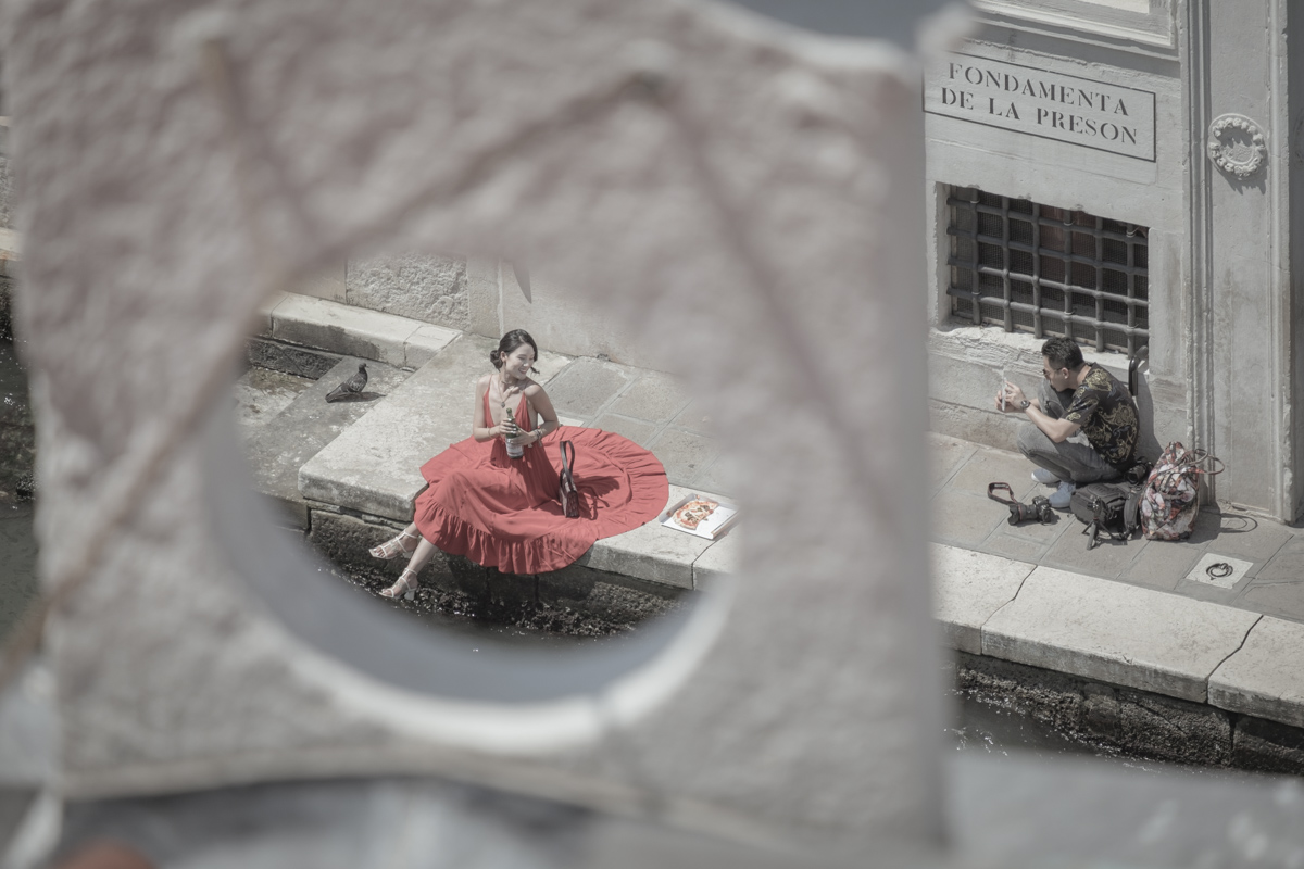 An Asian model poses for a photo shoot along Venice's Grand Canal, near the Rialto Bridge. The photo set re-enacts a stereotypical 'Italian scene', including a waterside pizza picnic, an Italian water bottle and a designer handbag.